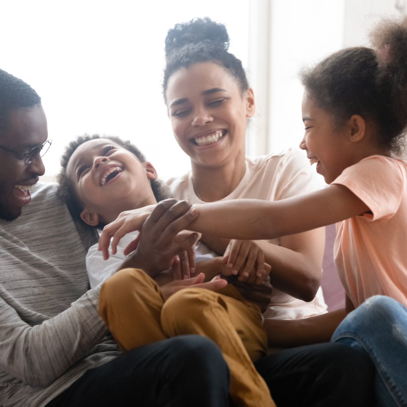 Overjoyed young family with little kids have fun playing relaxing on sofa in living room, happy biracial parents entertain with small children tickle laugh, enjoy weekend together