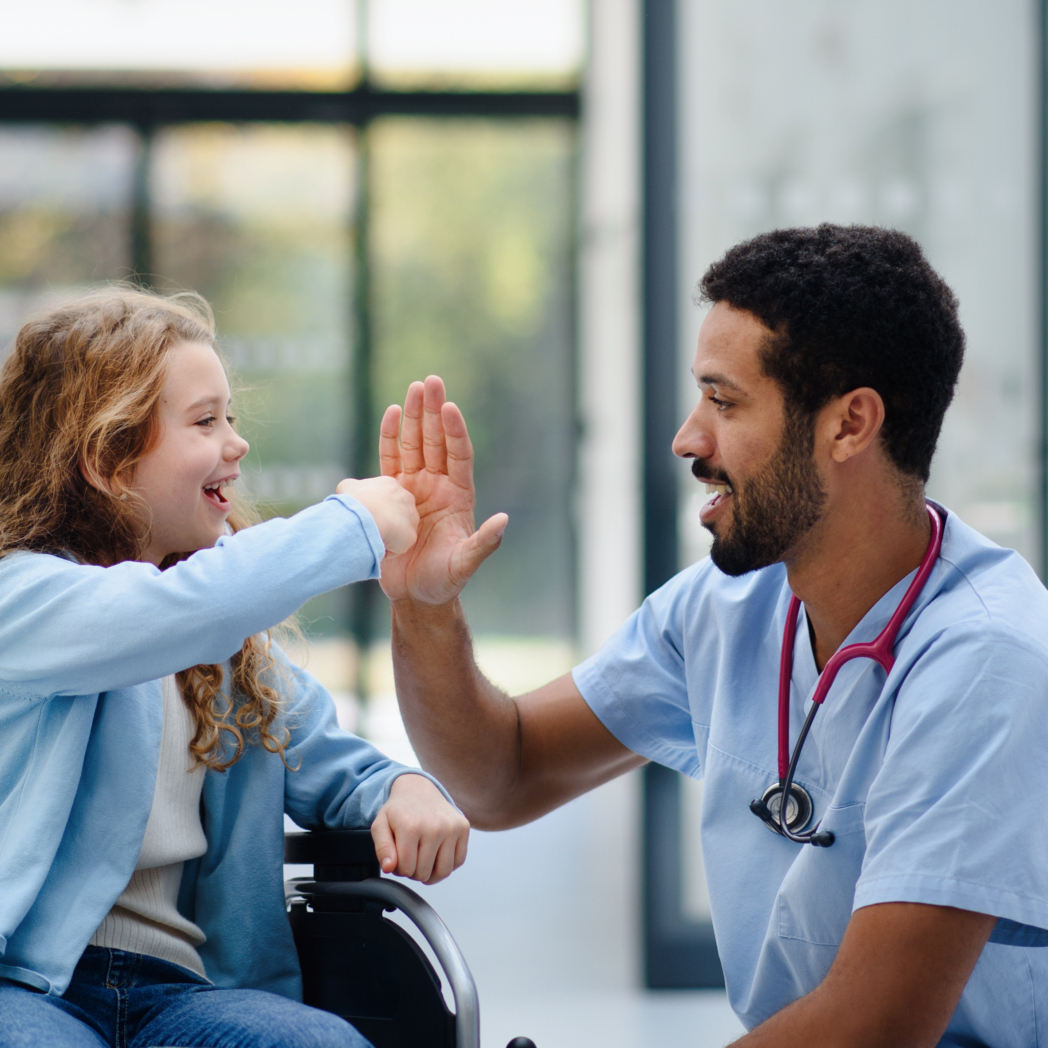 Young multiracial doctor having fun with little girl on a wheelchair.